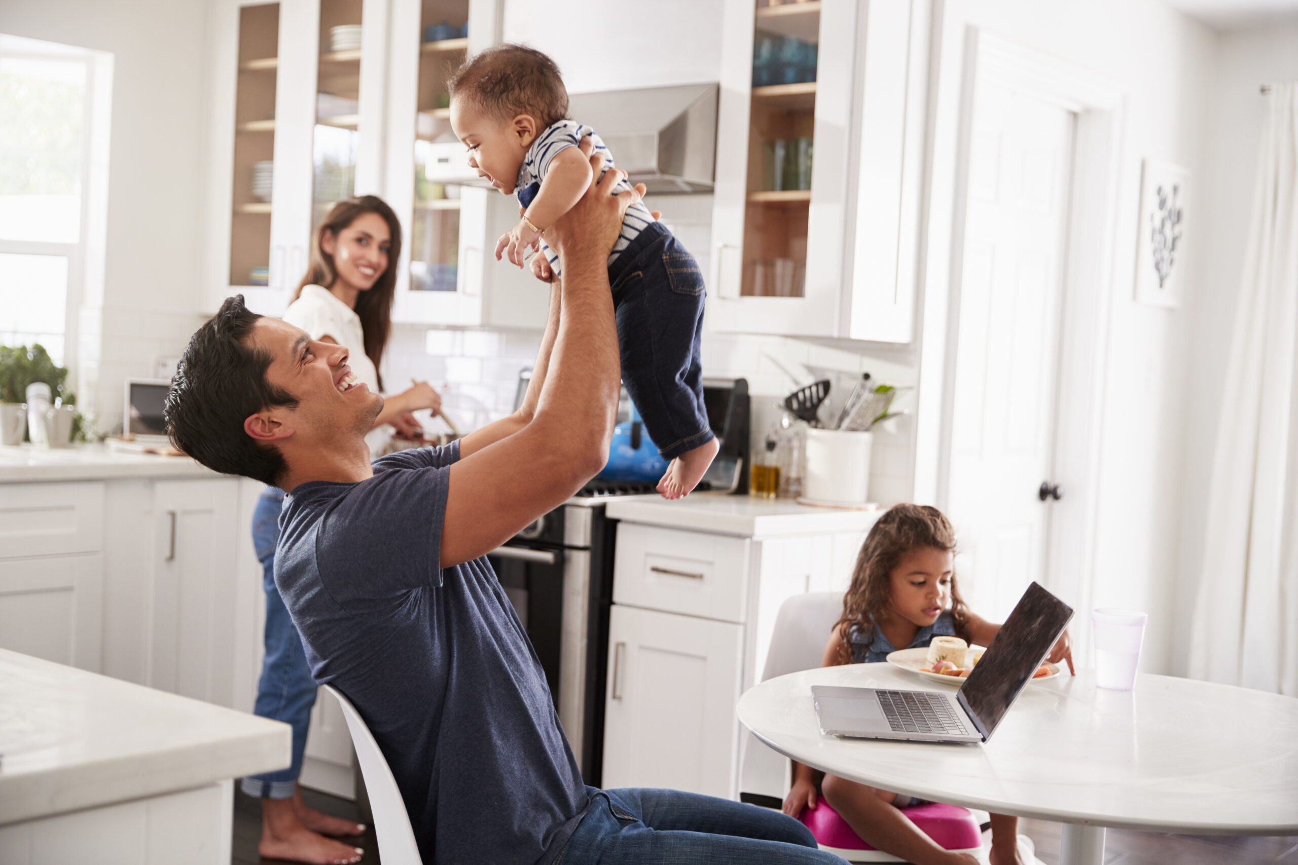Young family in their kitchen, dad lifting baby in the air