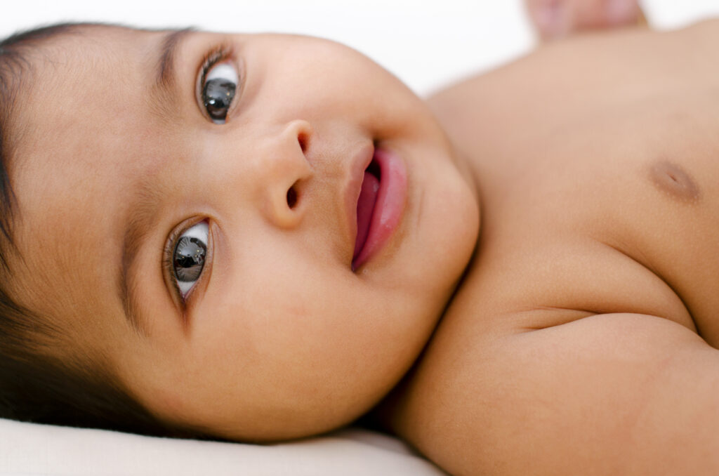 6 months old baby girl smiling, lying on bed.